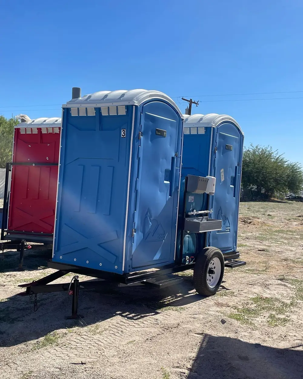 Porta potties strapped to a transport trailer in an open field